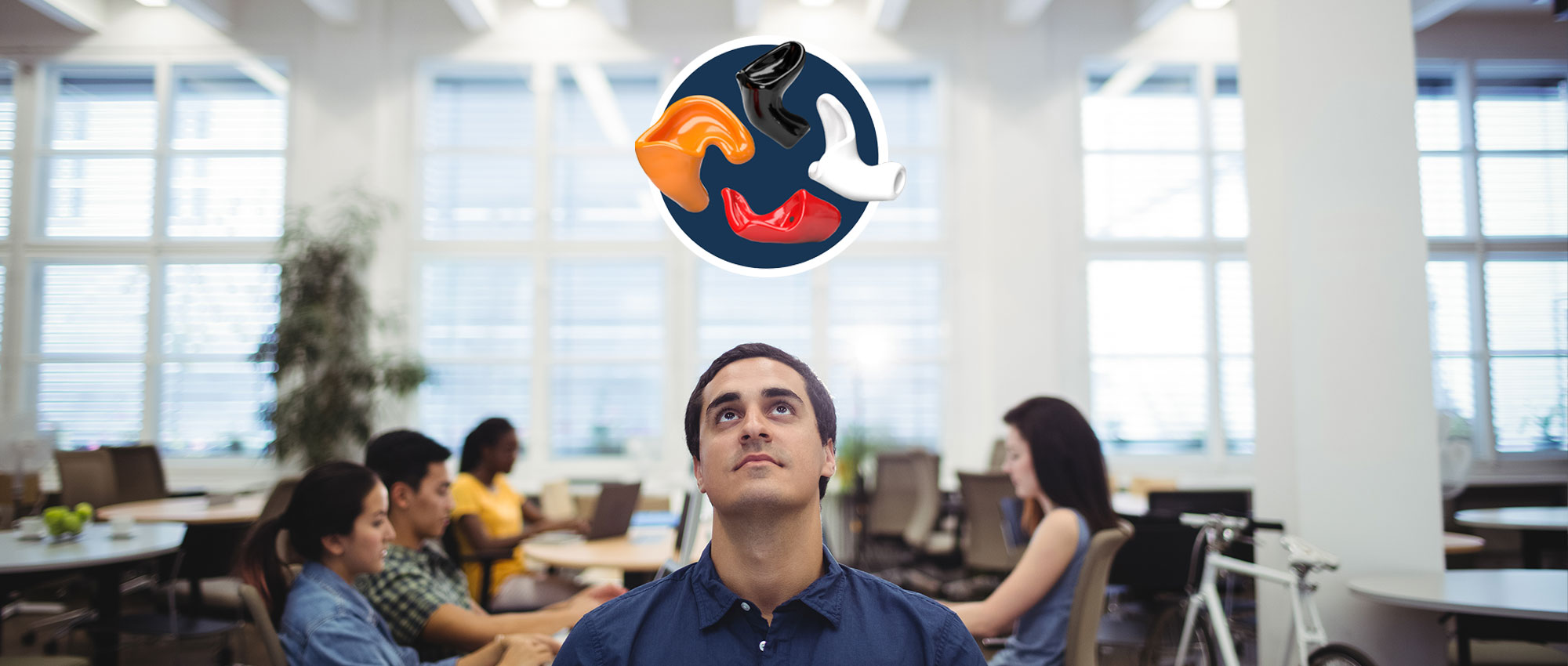 Mann sitzt im Büro mit Kollegen, darüber bunte Gehörschutzstöpsel als Symbol für Lärmschutz am Arbeitsplatz.​​​​​​​​​​​​​​​​​​​​​​​​​​​​​​​​​​​​​