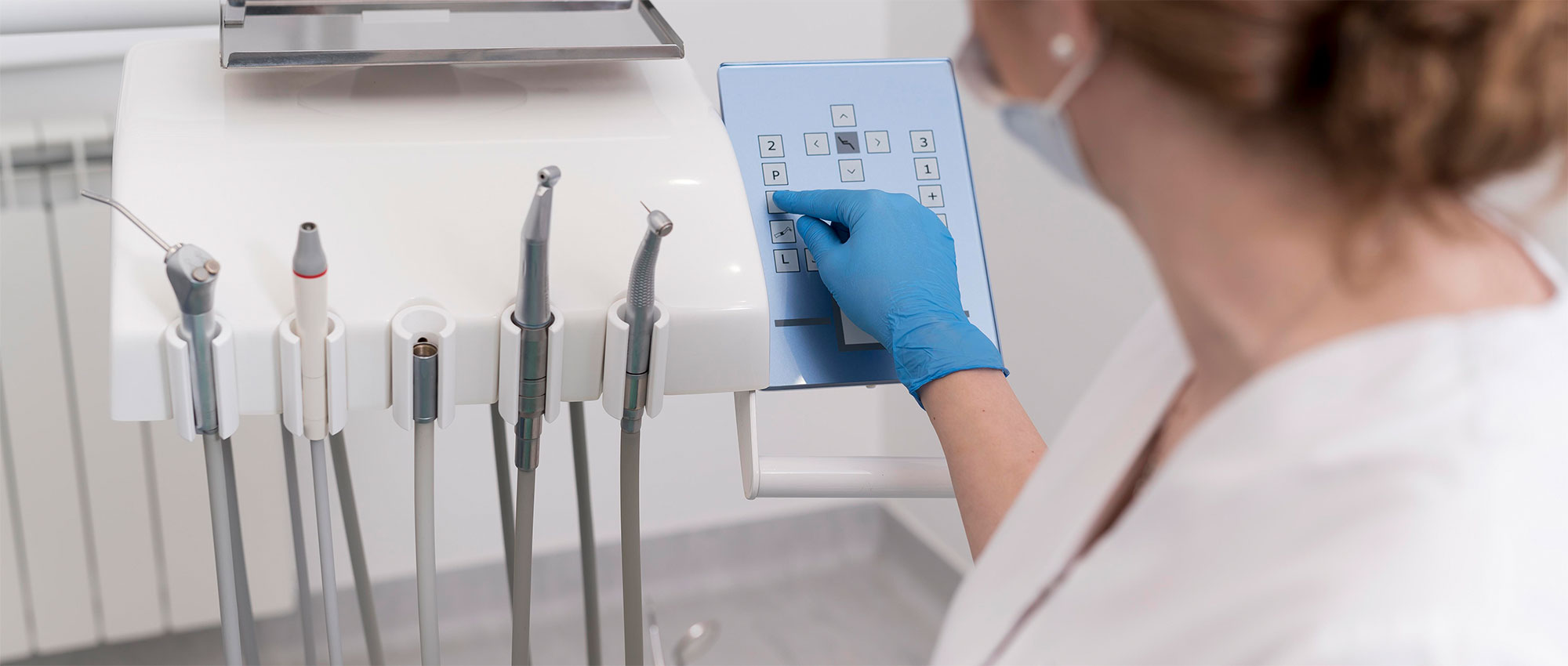 Zahnarzthelferin mit blauen Handschuhen bedient Steuerung an zahnärztlichem Gerät mit Bohrer im Behandlungsraum​​​​​​​​​​​​​​​​​​​​​​​​​​​​​​​​​​