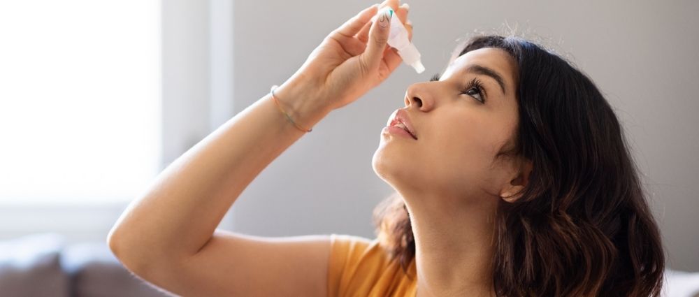 Junge Frau verwendet Augentropfen gegen Allergie in hellem Raum, Fokus auf Augenpflege und Linderung.​​​​​​​​​​​​​​​​​​​​​​​​​​​​​​​​​​​​​​​​​​​​