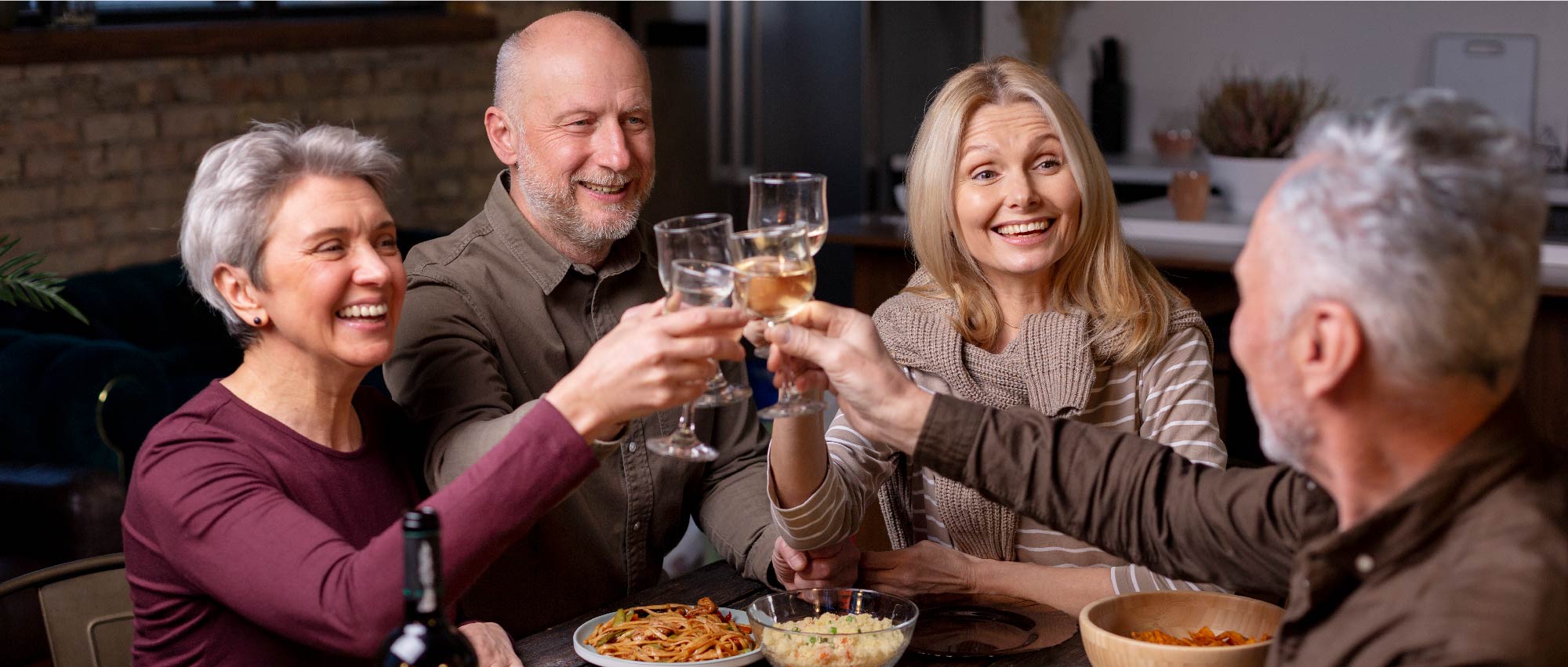 Vier ältere Menschen feiern gemeinsam mit Wein und Wasser bei einem gemütlichen Abendessen in entspannter Atmosphäre​​​​​​​​​​​​​​​​​​​​​​​​​​​​​