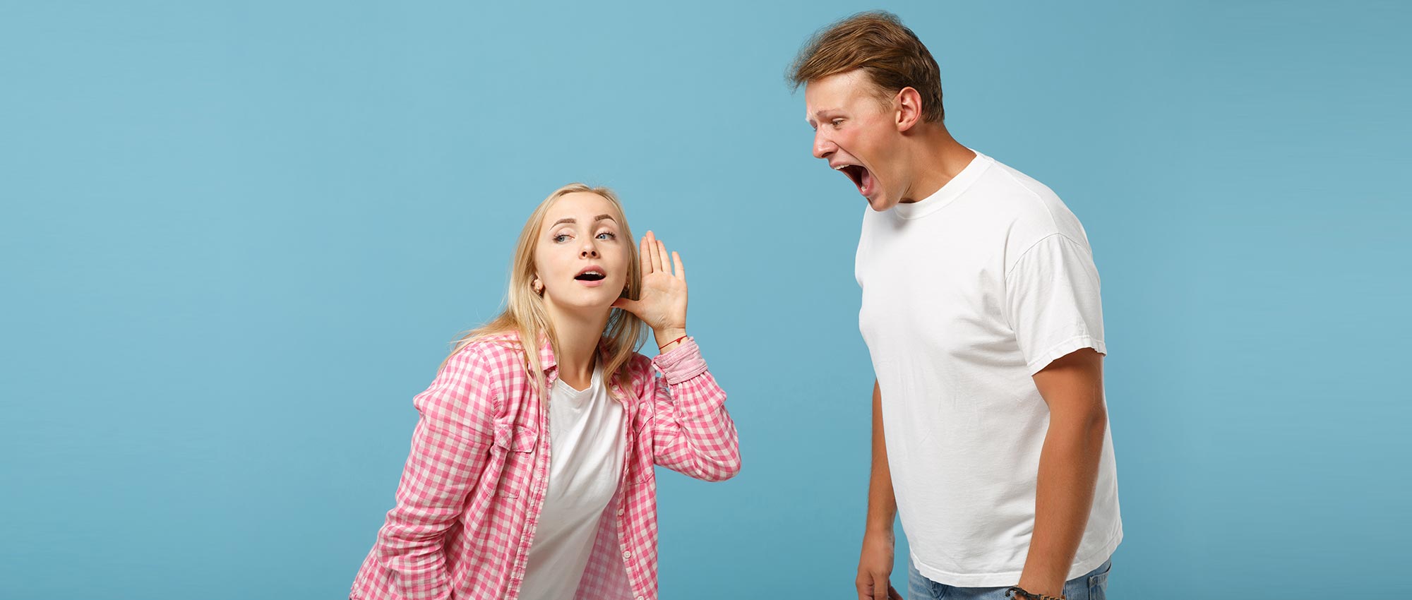 Junge Frau hält Hand ans Ohr und hört Mann zu, der laut spricht. Szene vor blauem Hintergrund mit Fokus auf Hörverständnis.​​​​​​​​​​​​​​​​​​​​​​