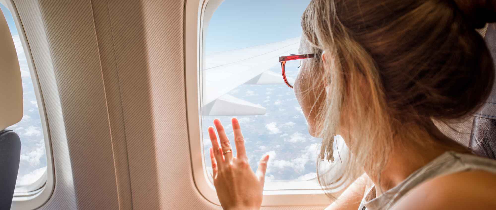 Frau mit roter Brille blickt aus Flugzeugfenster auf Wolken und Tragfläche während des Flugs​​​​​​​​​​​​​​​​​​​​​​​​​​​​​​​​​​​​​​​​​​​​​​​​​​​​​