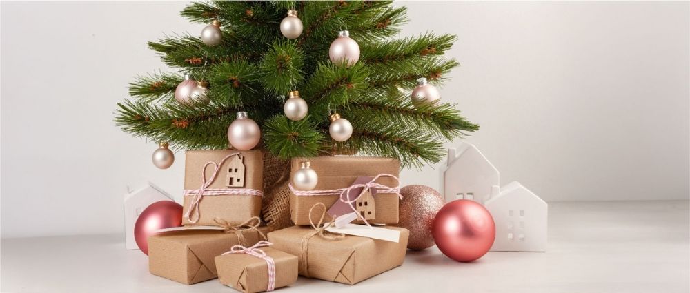 Kleiner Weihnachtsbaum mit rosa und beigen Kugeln, umgeben von verpackten Geschenken und weißen Deko-Häusern​​​​​​​​​​​​​​​​​​​​​​​​​​​​​​​​​​​​​