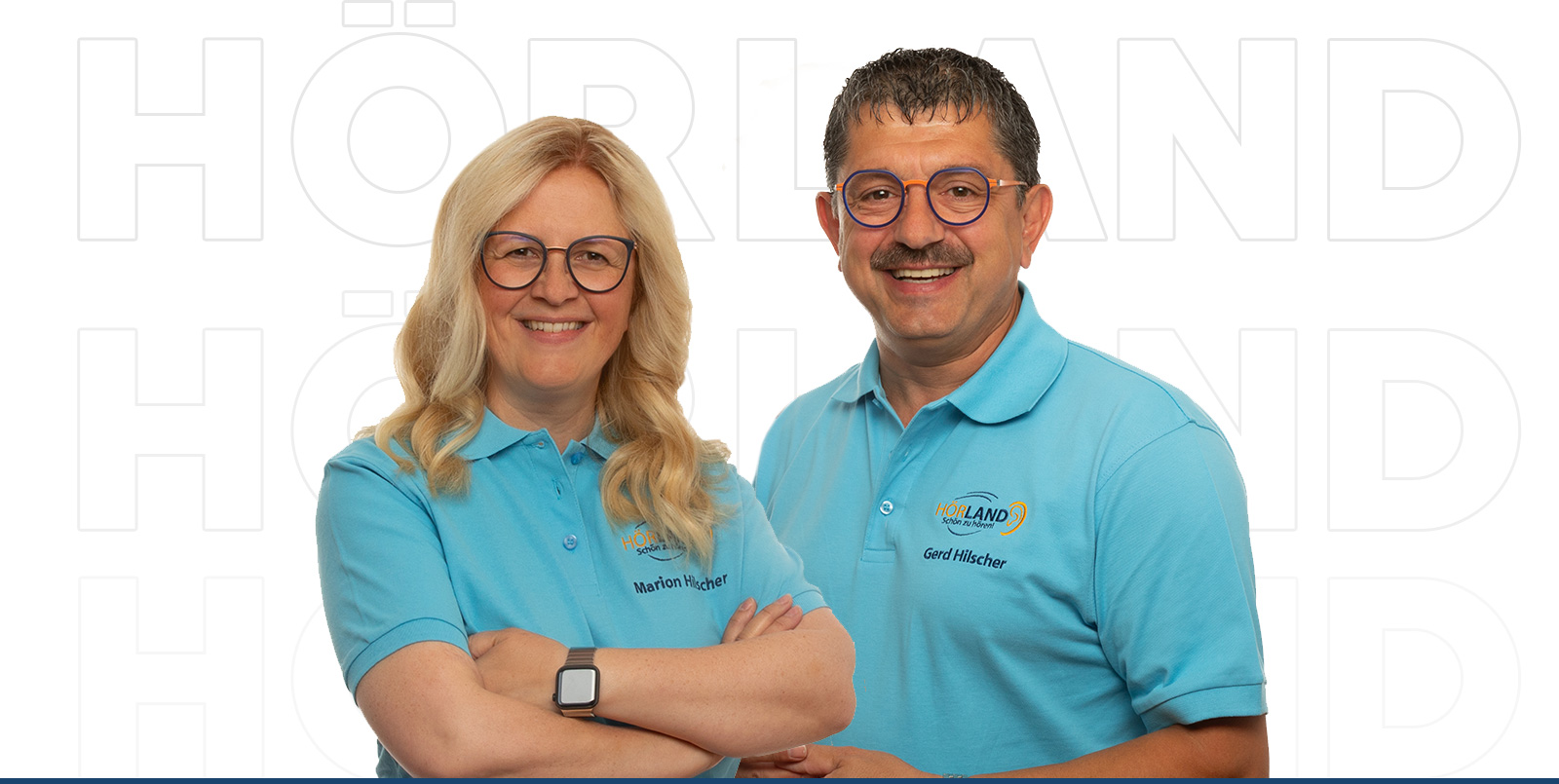 Zwei Hörakustiker mit blauen Poloshirts und Brillen lächeln vor weißem Hintergrund, professionell und freundlich​​​​​​​​​​​​​​​​​​​​​​​​​​​​​​​​​