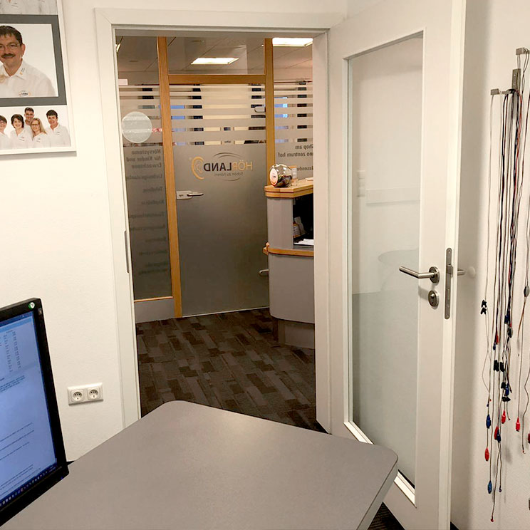 Blick in ein Hörakustikerbüro mit Empfangstresen, Messgeräten und Tür mit Firmenlogo in moderner Praxis​​​​​​​​​​​​​​​​​​​​​​​​​​​​​​​​​​​​​​​​​​