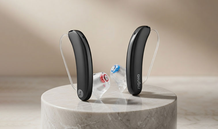 Zwei schwarze Hörgeräte mit transparenten Ohrstücken stehen auf einer runden Marmorplatte vor hellem Hintergrund​​​​​​​​​​​​​​​​​​​​​​​​​​​​​​​​​