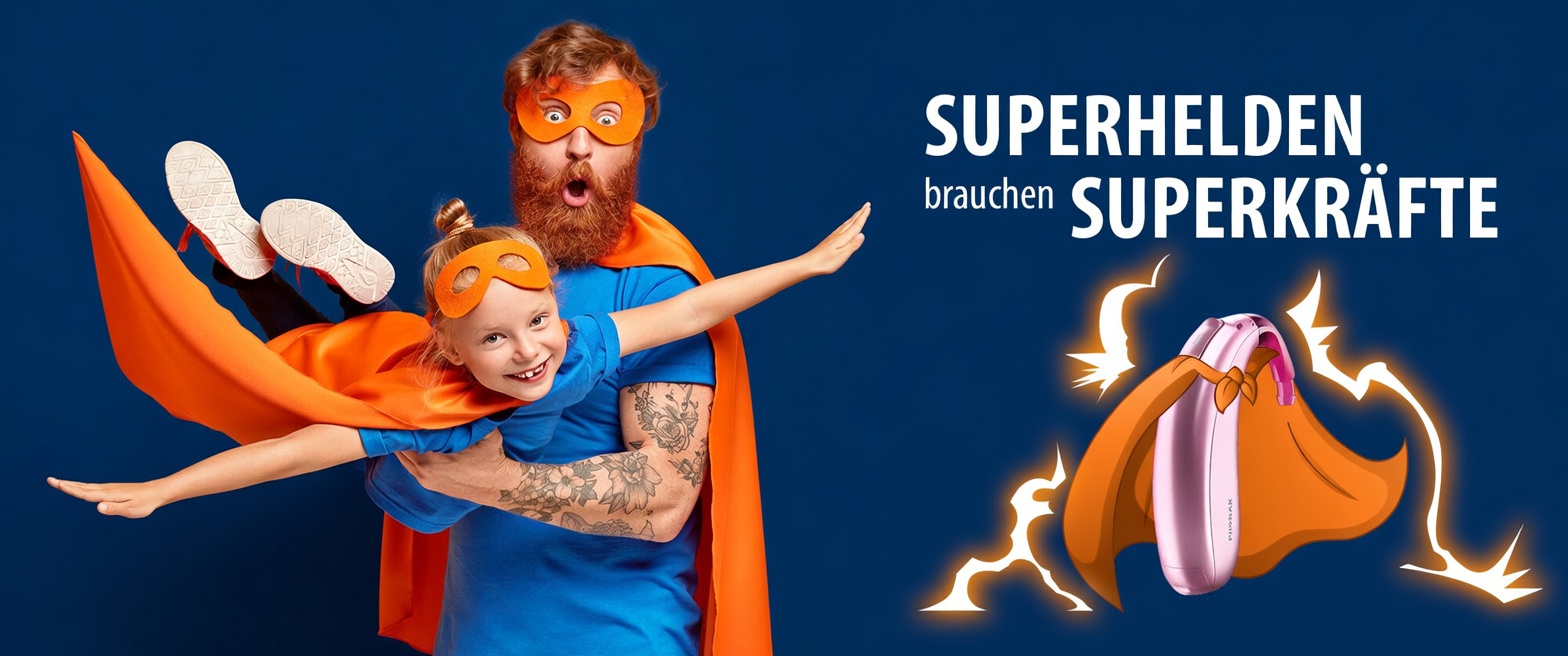 Vater und Tochter als Superhelden mit Hörgerät und orangen Umhängen vor blauem Hintergrund.​​​​​​​​​​​​​​​​​​​​​​​​​​​​​​​​​​​​​​​​​​​​​​​​​​​​​​
