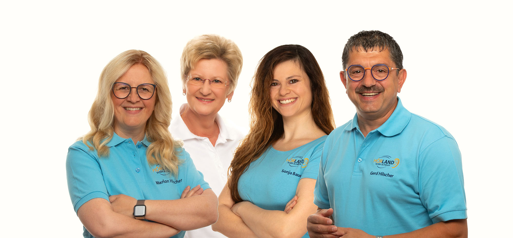 Vier lächelnde Personen in HÖRLAND Polohemden posieren vor weißem Hintergrund, Teamfoto mit freundlicher Atmosphäre​​​​​​​​​​​​​​​​​​​​​​​​​​​​​​