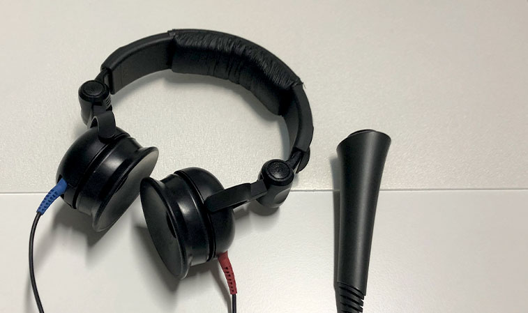 Schwarze Kopfhörer mit farbigen Kabeln und ein Hörtest-Messgerät liegen auf einem weißen Tisch in ruhiger Umgebung.​​​​​​​​​​​​​​​​​​​​​​​​​​​​​​
