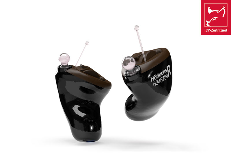 Zwei schwarze Hörgeräte mit Seriennummer und ICP-Zertifikat vor weißem Hintergrund, Nahaufnahme der Technik.​​​​​​​​​​​​​​​​​​​​​​​​​​​​​​​​​​​​​
