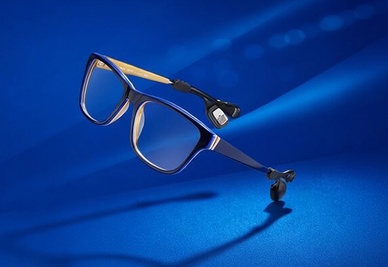 Blaue Brille mit Knochenleitungshörgerät auf blauem Hintergrund, modernes Design und technische Details sichtbar.​​​​​​​​​​​​​​​​​​​​​​​​​​​​​​​​