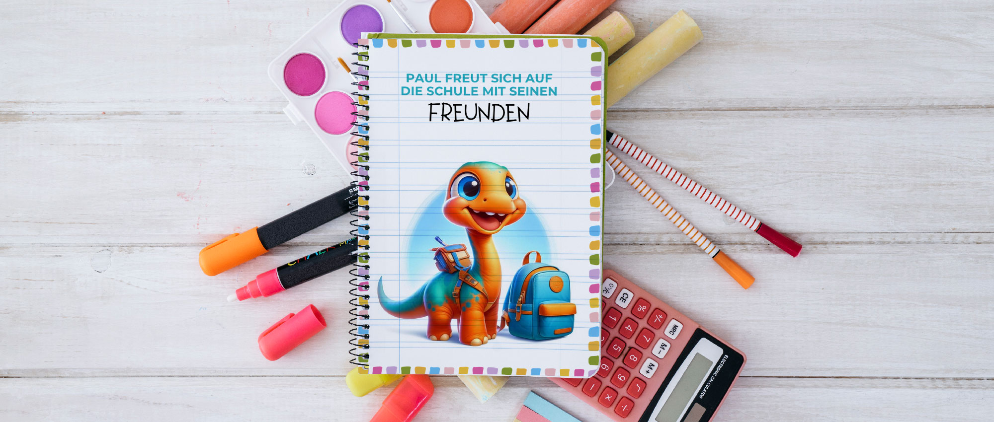 Notizbuch mit fröhlichem Dinosaurier und Schulranzen umgeben von Stiften, Kreide und Taschenrechner für Schulstart​​​​​​​​​​​​​​​​​​​​​​​​​​​​​​​