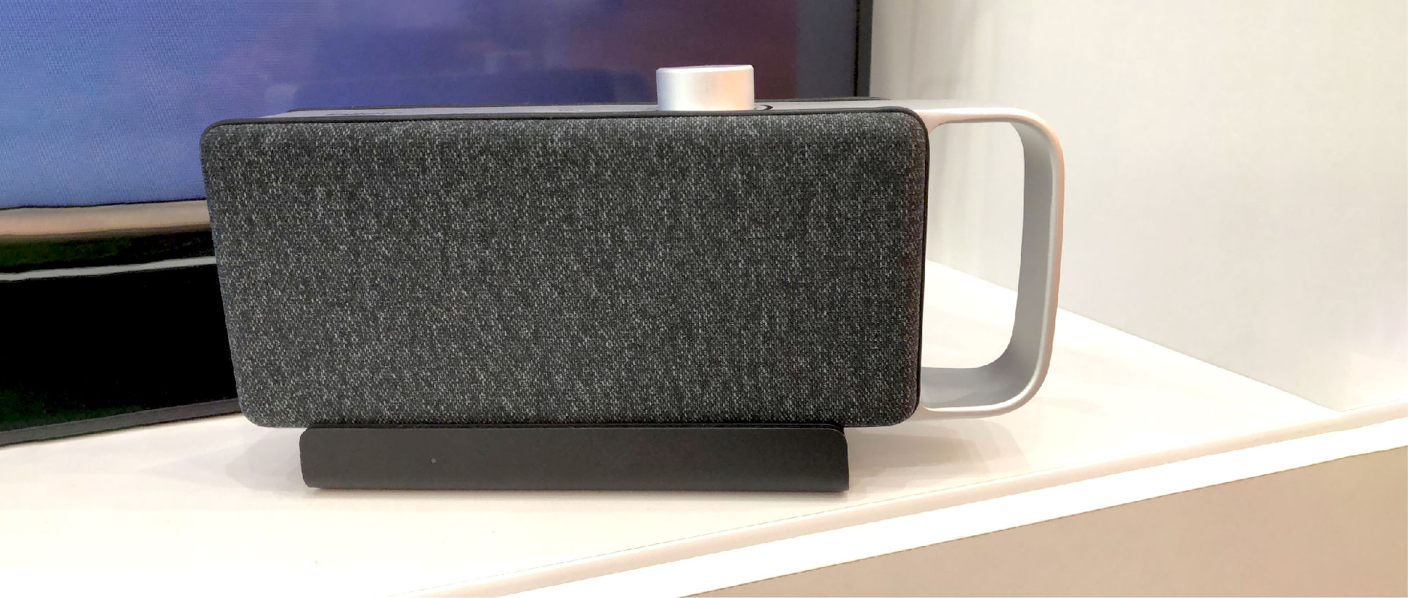 Moderner Lautsprecher mit grauer Stoffbespannung und weißem Tragegriff auf weißem Regal in Innenraum​​​​​​​​​​​​​​​​​​​​​​​​​​​​​​​​​​​​​​​​​​​​​