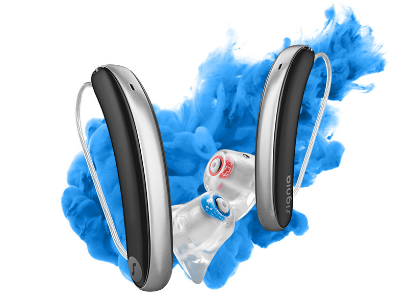 Nahaufnahme von Signia Hörgeräten mit transparenten Ohrpassstücken vor blauem Farbnebel. Moderne Hörtechnik sichtbar.​​​​​​​​​​​​​​​​​​​​​​​​​​​​