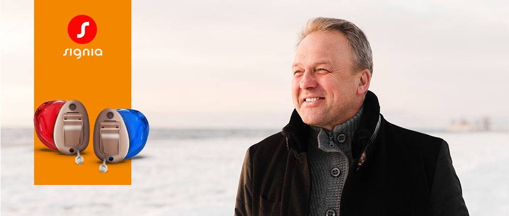 Älterer Mann trägt Signia Insio Charge Go CIC Hörgeräte, stehend vor verschneiter Landschaft bei Tageslicht.​​​​​​​​​​​​​​​​​​​​​​​​​​​​​​​​​​​​​