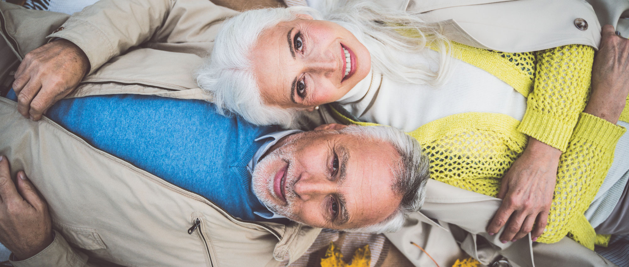 Älteres Paar mit grauen Haaren liegt nebeneinander auf Decke im Freien, trägt helle Kleidung und zeigt Nähe und Zufriedenheit​​​​​​​​​​​​​​​​​​​​