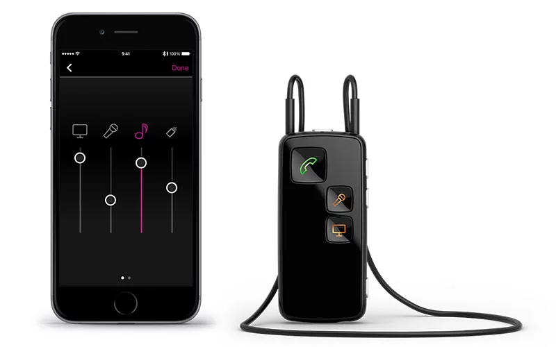 Ein schwarzer Streaming-Adapter neben einem Smartphone, das die Anpassung der Hörgeräteeinstellungen zeigt.