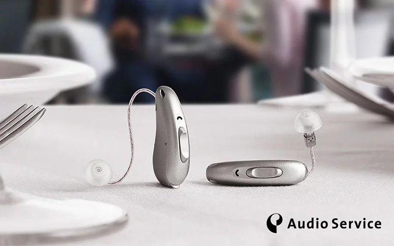 Zwei Hörgeräte von Audio Service liegen auf einer Tischdecke. Audio Service, hochwertige Hörgeräte, Hörakustik.