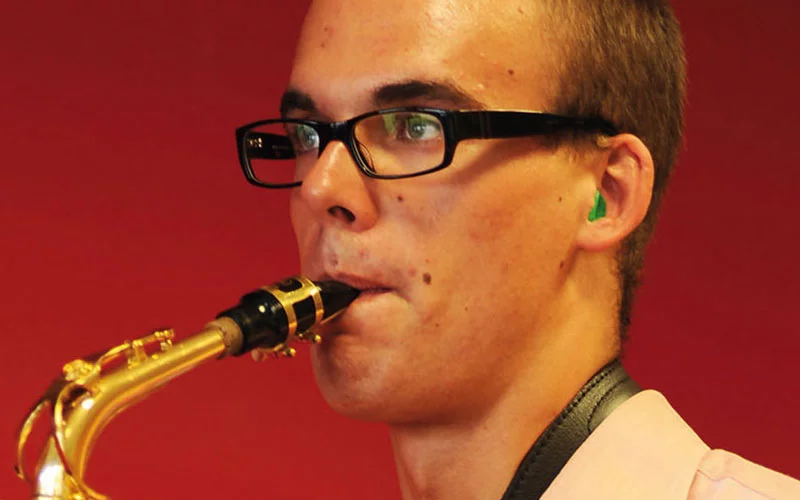 Mann mit grünem Hörschutz für Musiker spielt Saxophon.
