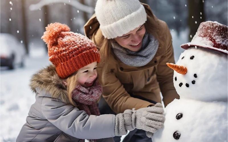 Mutter und Tochter bauen gemeinsam einen Schneemann an einem verschneiten Wintertag. Freude am Winterspaß, gutes Hören im Freien, Hörakustik im Schnee.